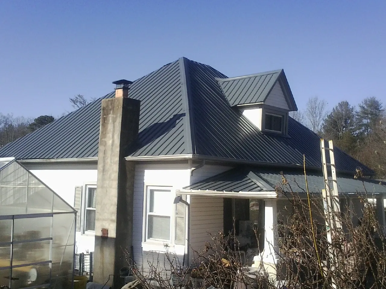 Dark blue standing seam metal roof on a white farmhouse with dormer — Slate & Tile Roof Repair by Roofing Brothers in Roxobel