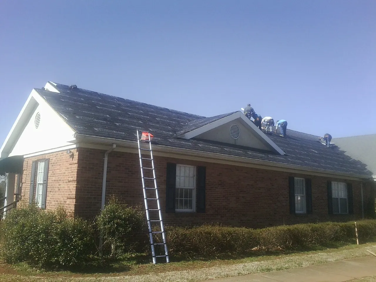 Crew tearing shingles off a brick ranch roof with a ladder set — Emergency Roof Repair work by our crew in Roxobel