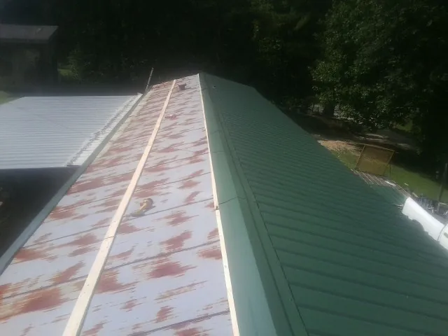 Old rusted panels beside newly installed green metal roofing — Wind Damage Roof Repair by Roofing Brothers in Roxobel