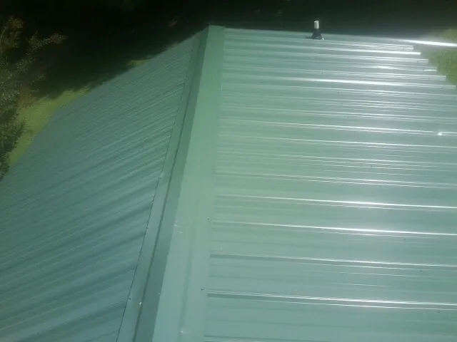 New green metal panels meeting at the ridge of a roof — Flat Roof Repair work by our crew in Roxobel