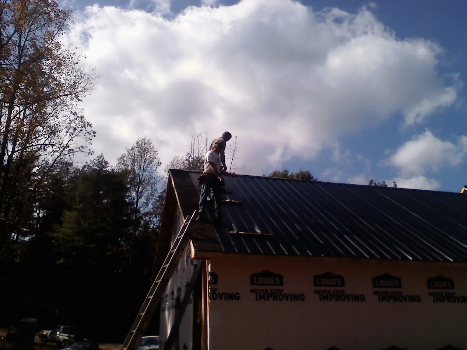 Roofer fastening dark metal panels high against a cloudy sky, from a Roof Inspection job in Roxobel