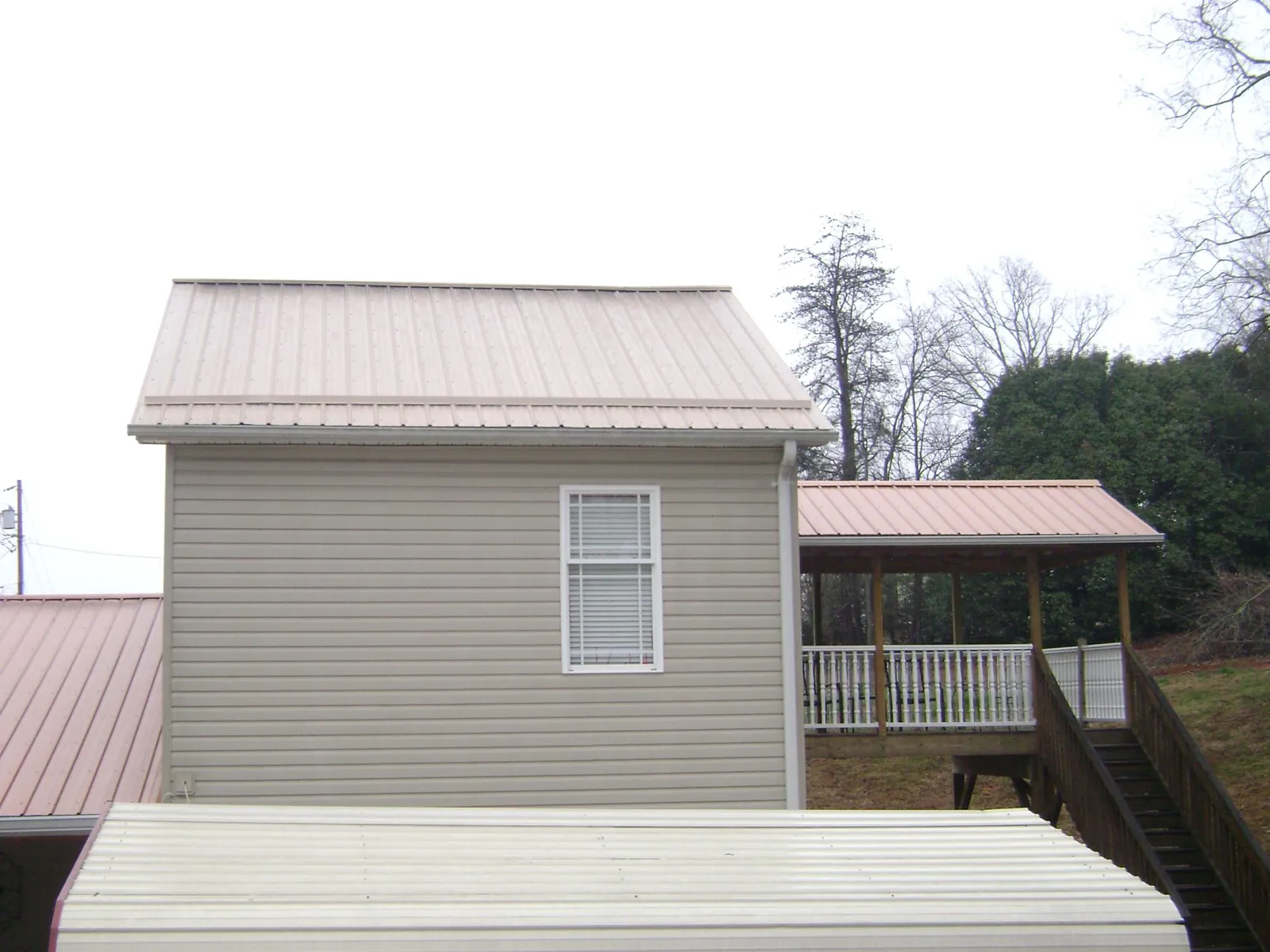 Tan metal roofs on a two story addition and attached porch, from a Roof Replacement job in Roxobel